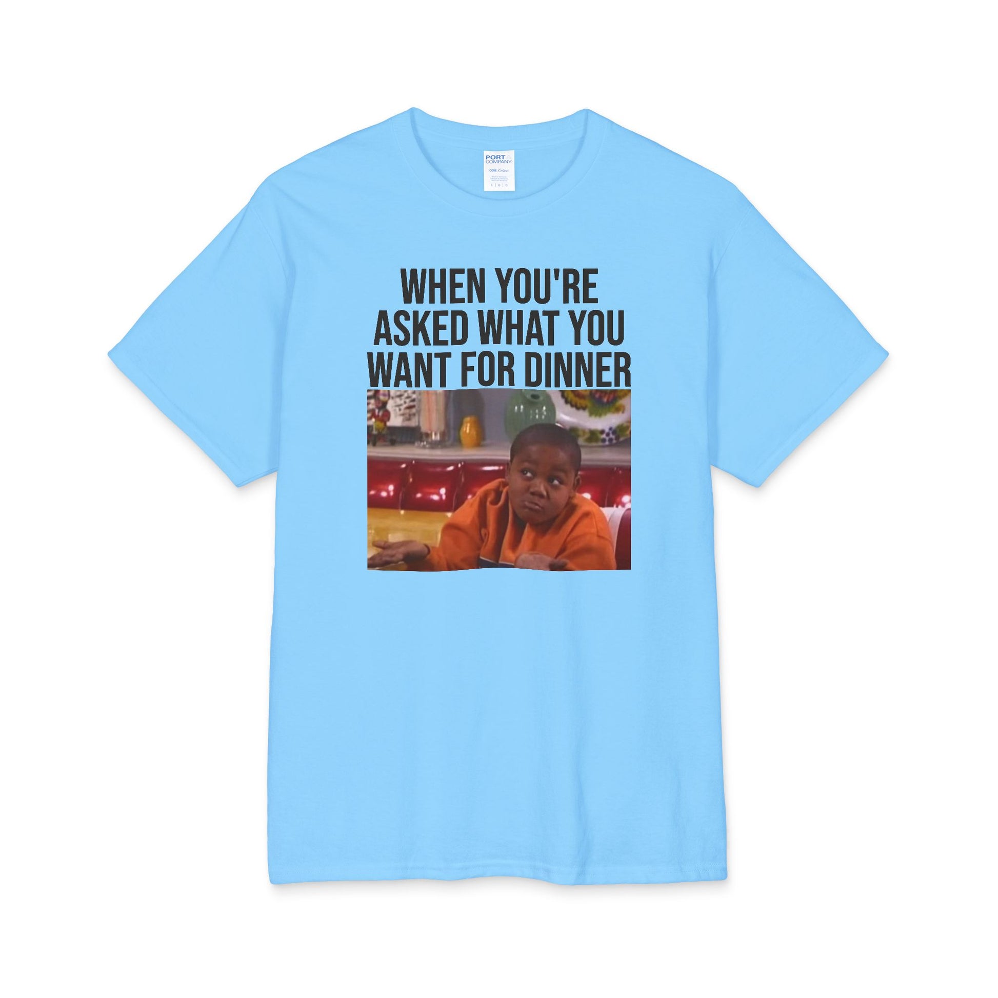 A light blue t-shirt with a graphic image of a boy shrugging and text above it stating 'When You're Asked What You Want For Dinner' on a white background