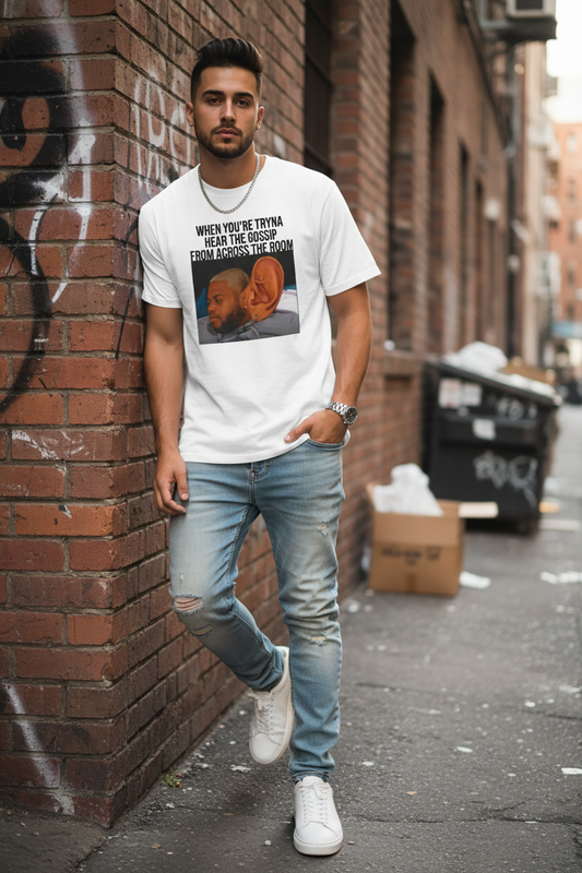 A man wearing a white t-shirt with graphic design of a man with a large ear and text above it stating 'When You're Tryna Hear The Gossip From Across The Room' leaning against a brick wall